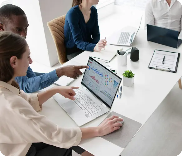 Team of four professionals collaborating around a bright conference table, a laptop displays charts and graphs.