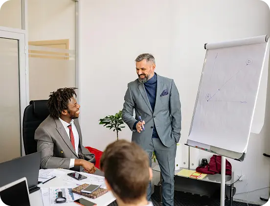 Man in a gray suit presents a line graph on a flip chart to two colleagues in a modern office. (informative)