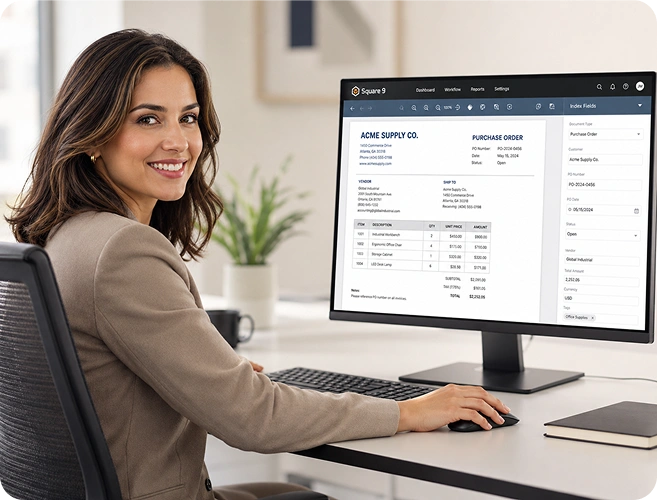 Smiling woman at a desk uses a desktop monitor showing an invoice in accounting software.